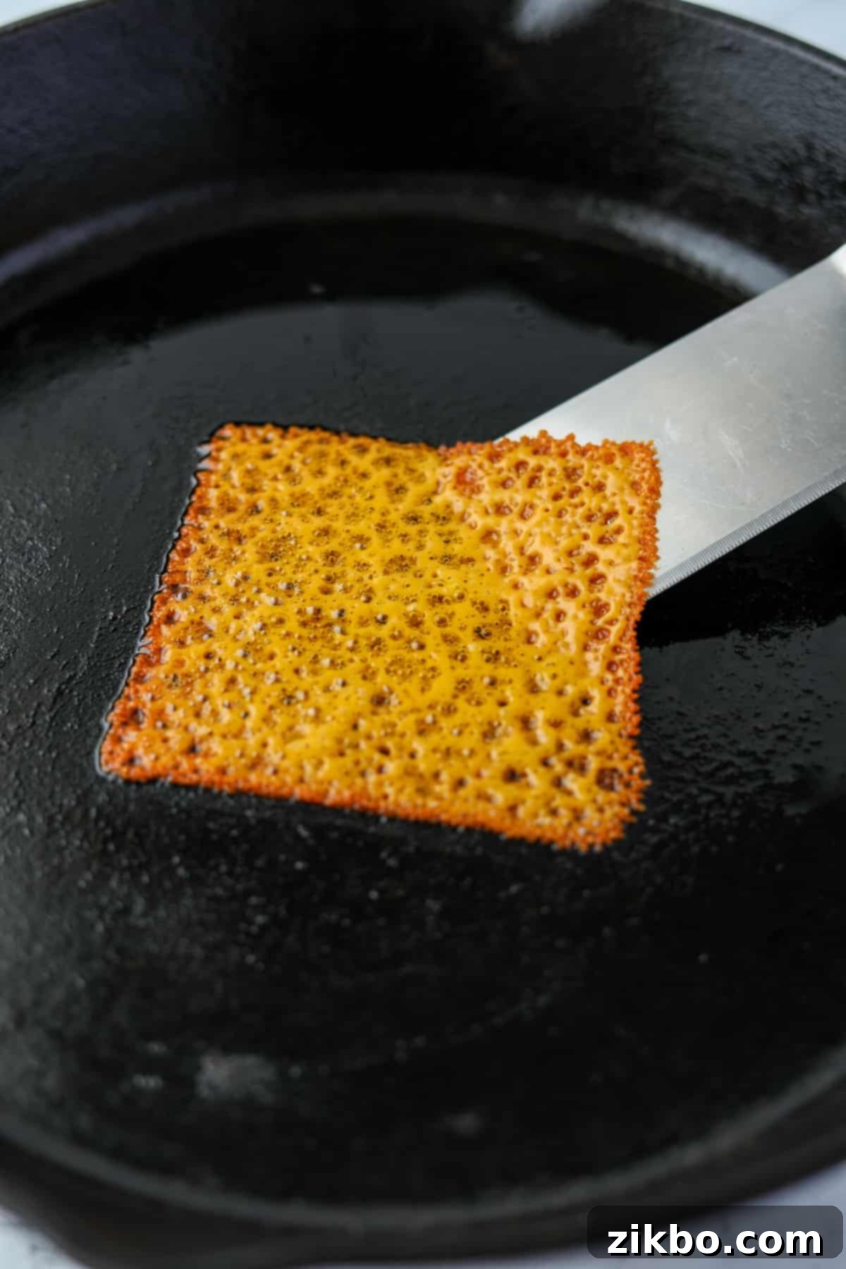 Using a spatula to loosen a melted cheese slice from a spatula.