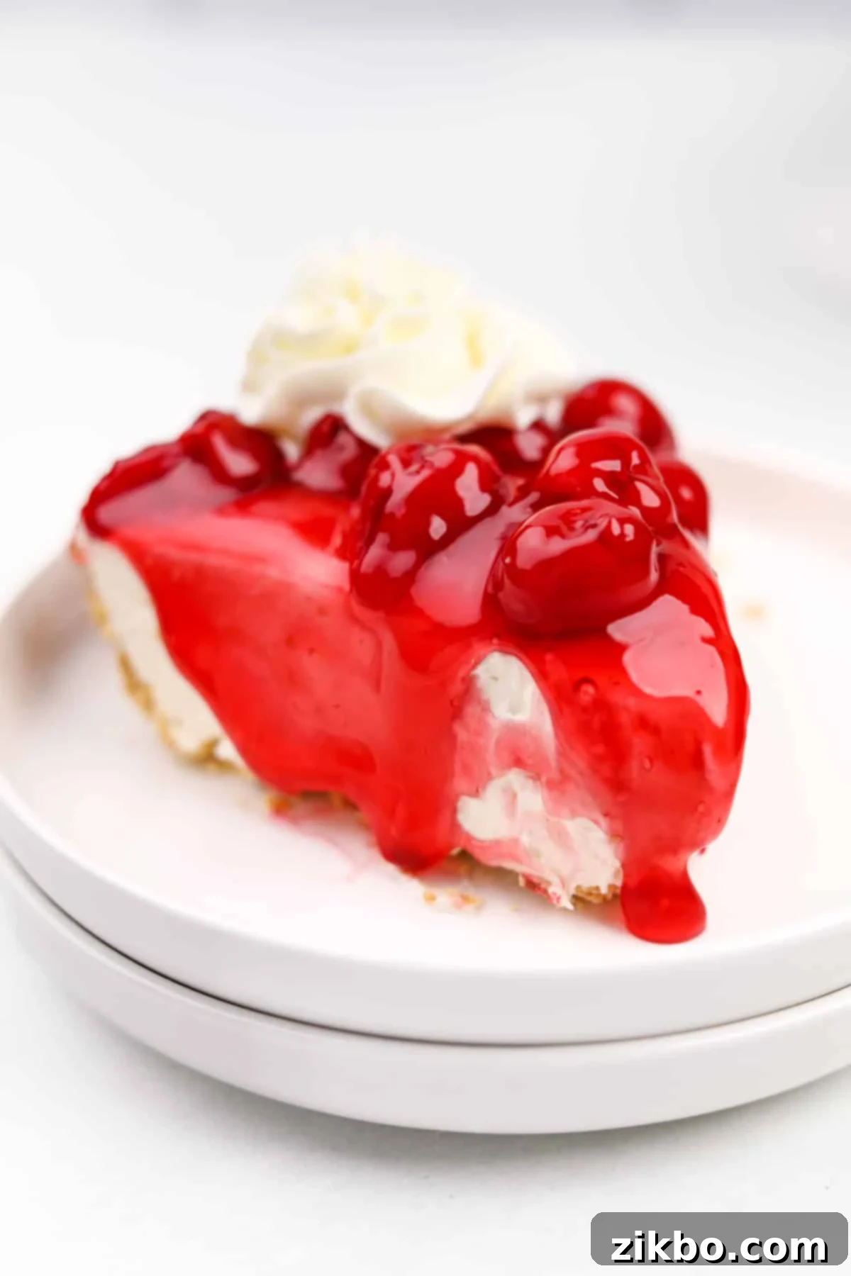 A beautiful slice of no-bake cheesecake with cherry topping and a swirl of whipped cream.