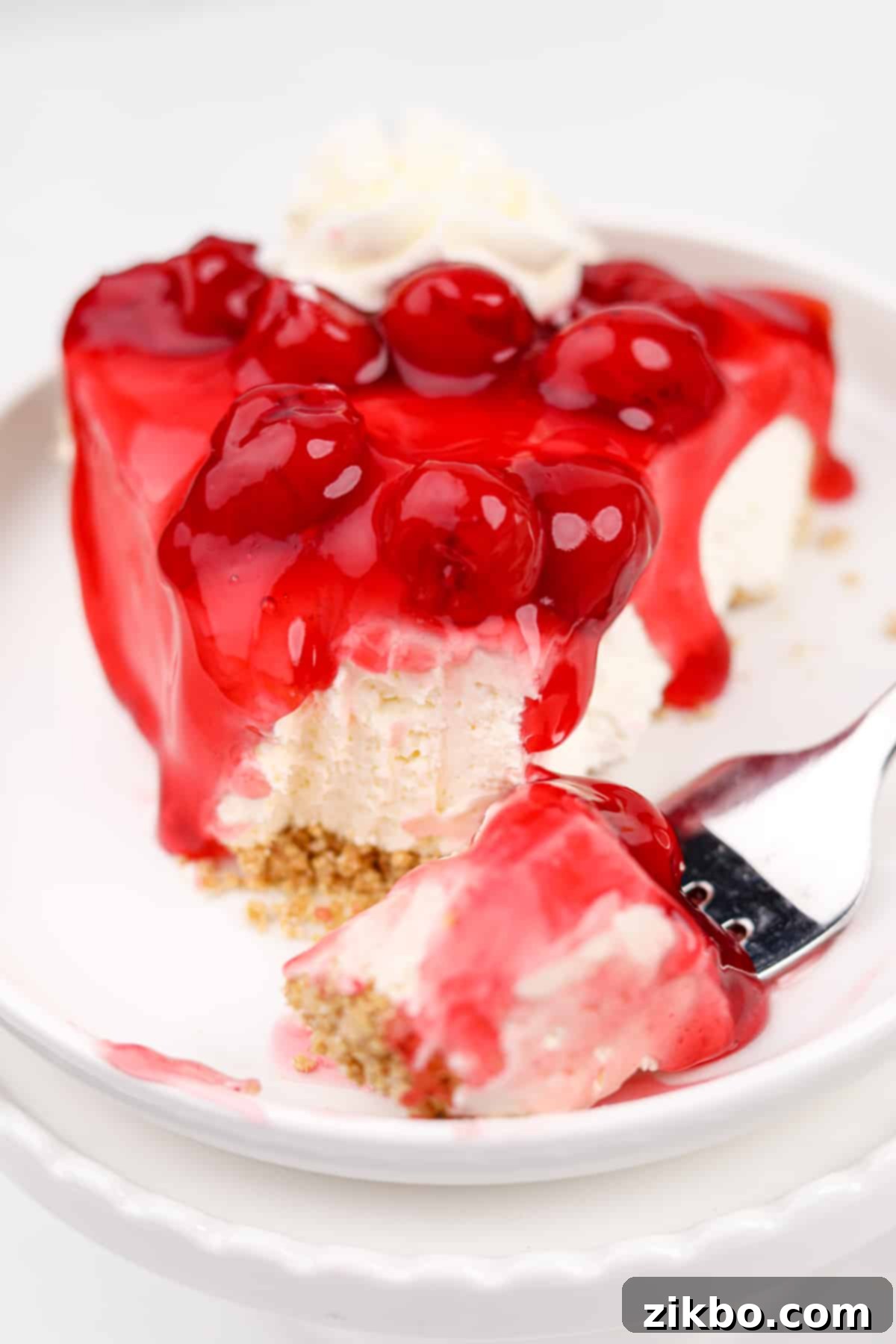 A close-up view of a slice of no-bake cheesecake pie, glistening with a cherry glaze on top.