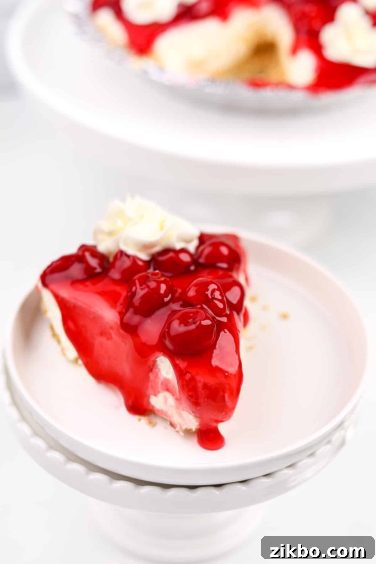 A vibrant slice of no-bake cheesecake, generously topped with glistening cherries and a rich glaze.