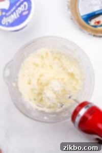 An electric mixer blending cream cheese with sugar.