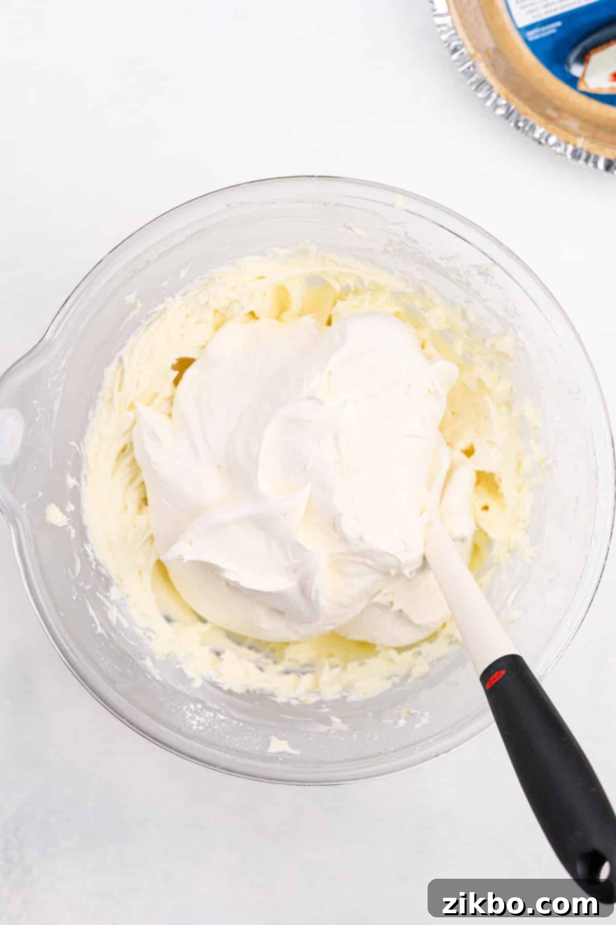 Thawed whipped topping being added to the creamy cream cheese and sugar mixture in a large bowl.