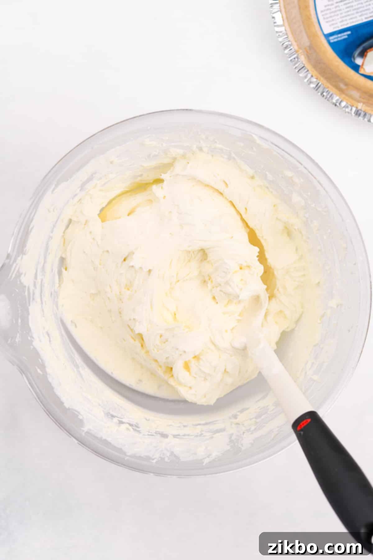 A rubber spatula gently stirring the cheesecake filling, ensuring the whipped topping is fully incorporated.