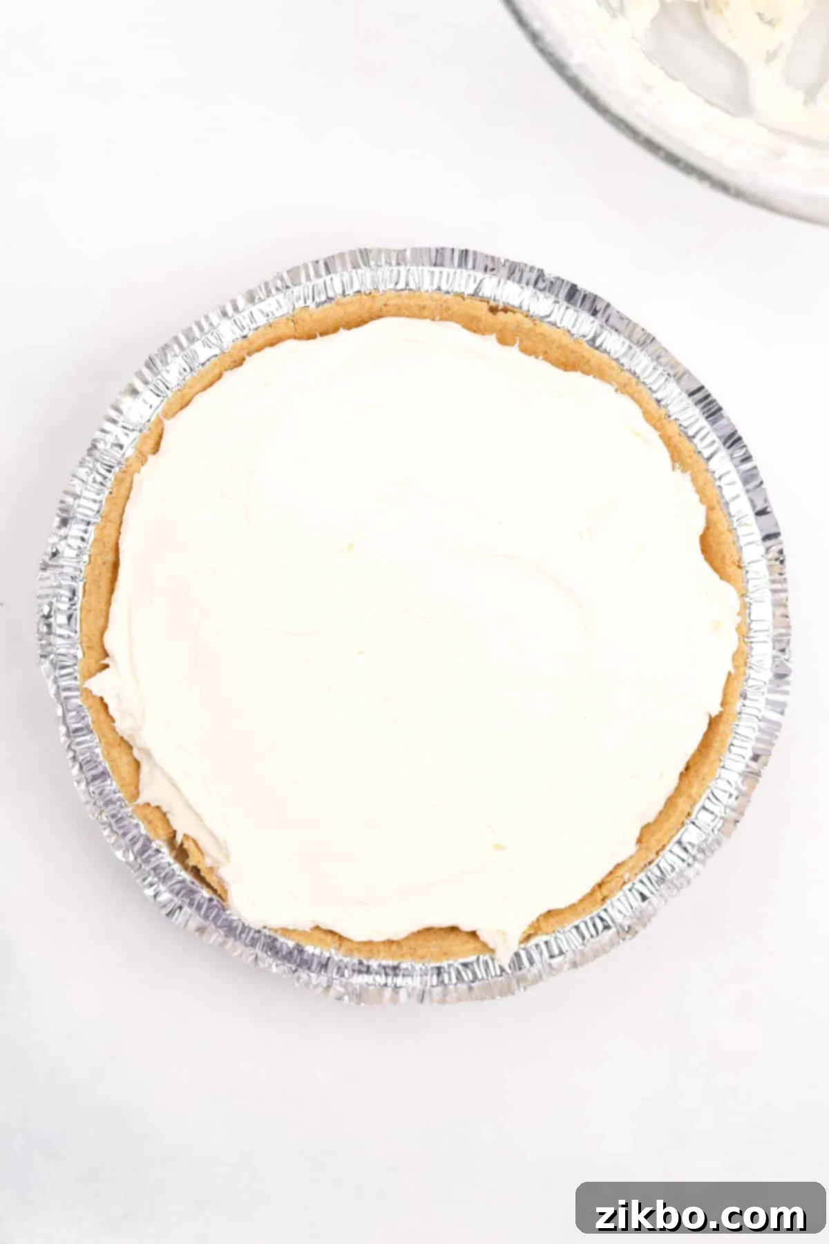 A pre-made graham cracker pie crust filled with the creamy, white cheesecake mixture, smoothed evenly.