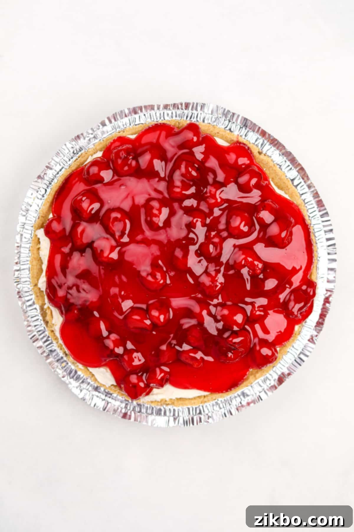 A fully chilled cheesecake pie generously topped with a rich, glossy layer of cherry pie filling.