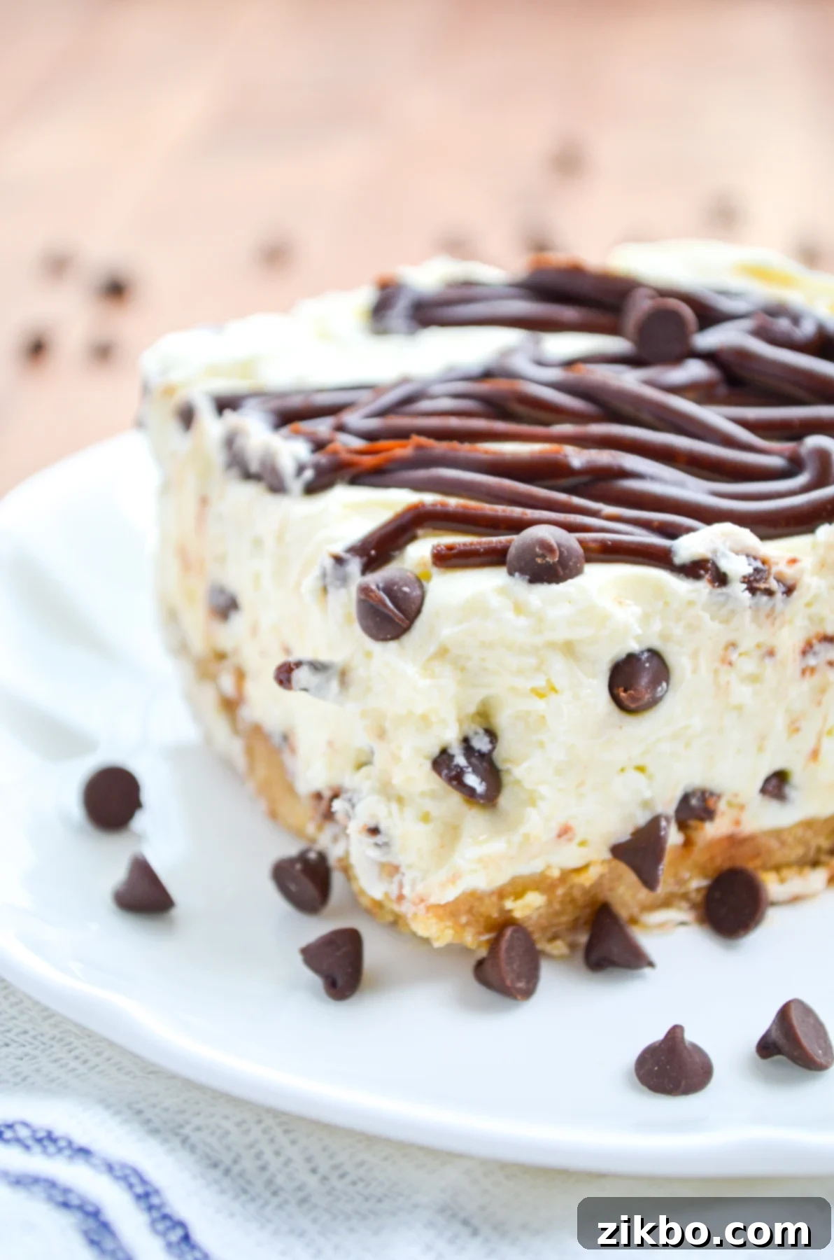 A close-up of a slice of no bake chocolate chip cheesecake, showcasing the rich chocolate ganache drizzle and mini chocolate chips.
