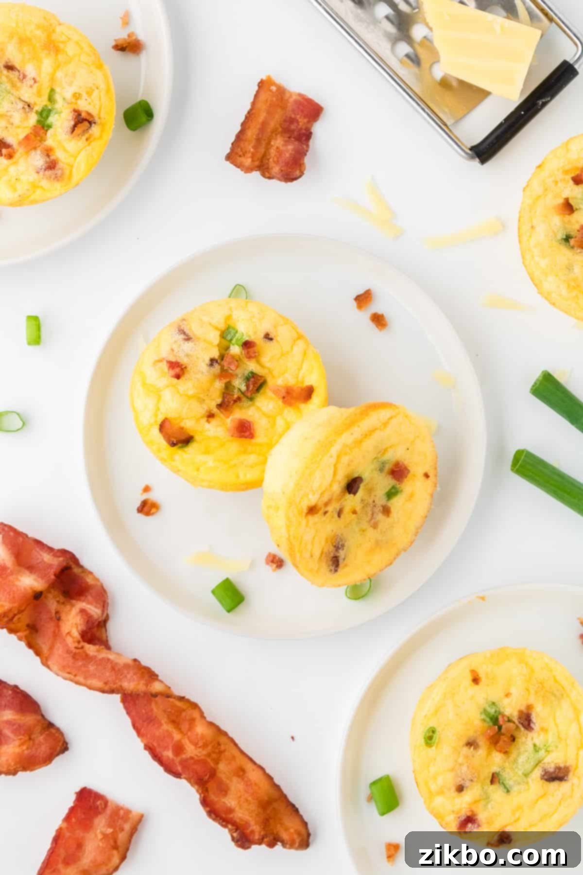 Copycat Starbucks Bacon and Gruyere Egg Bites 2 Two egg bites on a white plate, surrounded by more egg bites and strips of bacon.