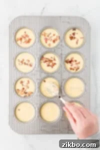 Pressing bacon down under an egg-based batter in a muffin pan.