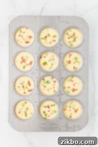 A muffin pan with all of the wells filled with an egg and bacon mixture and sprinkled with green onions.