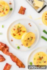 Two egg bites on a white plate, surrounded by more egg bites and strips of bacon.