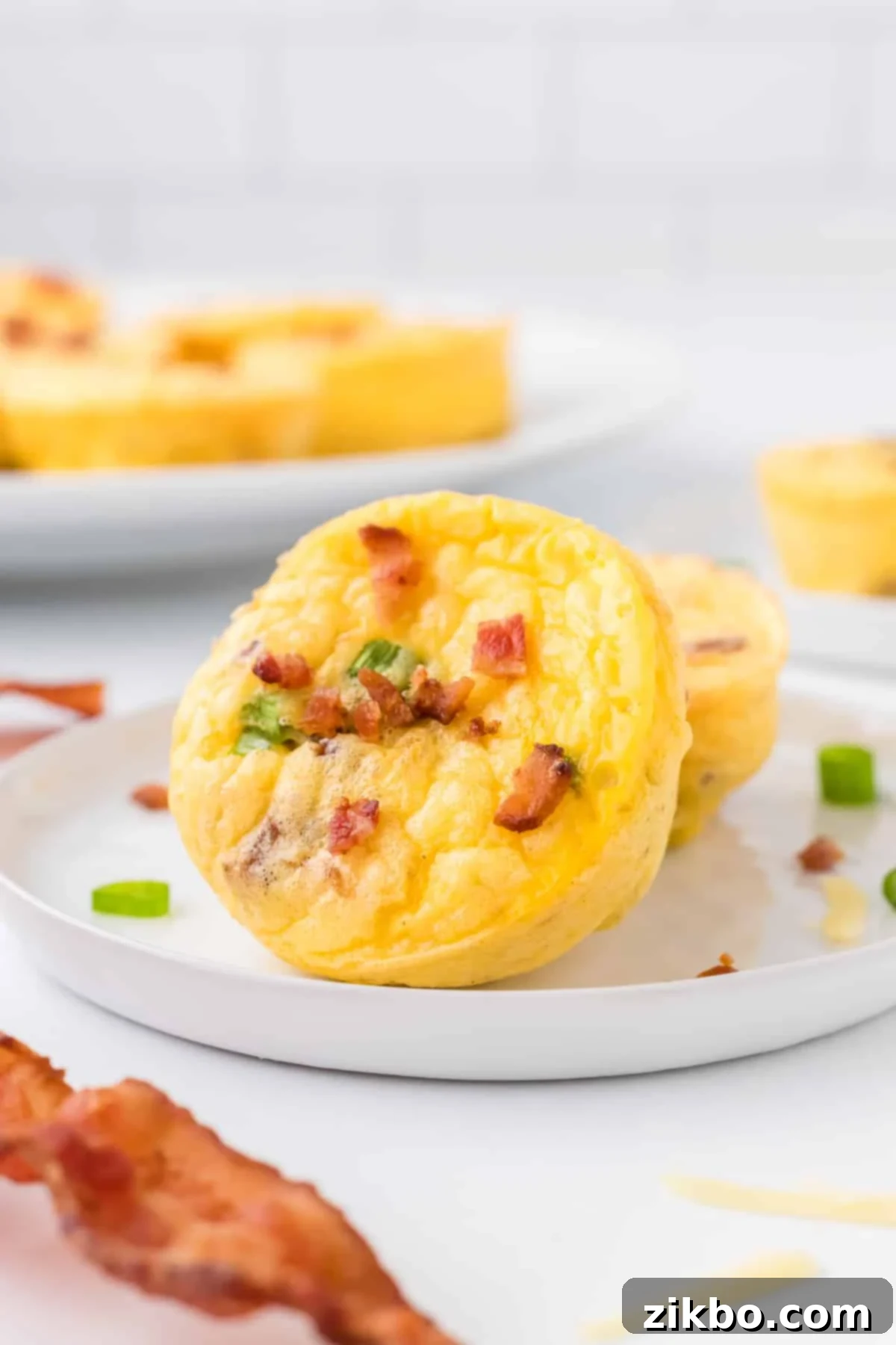 Copycat Starbucks Bacon and Gruyere Egg Bites 7 Two egg bites on a plate garnished with cooked bacon and green onion.