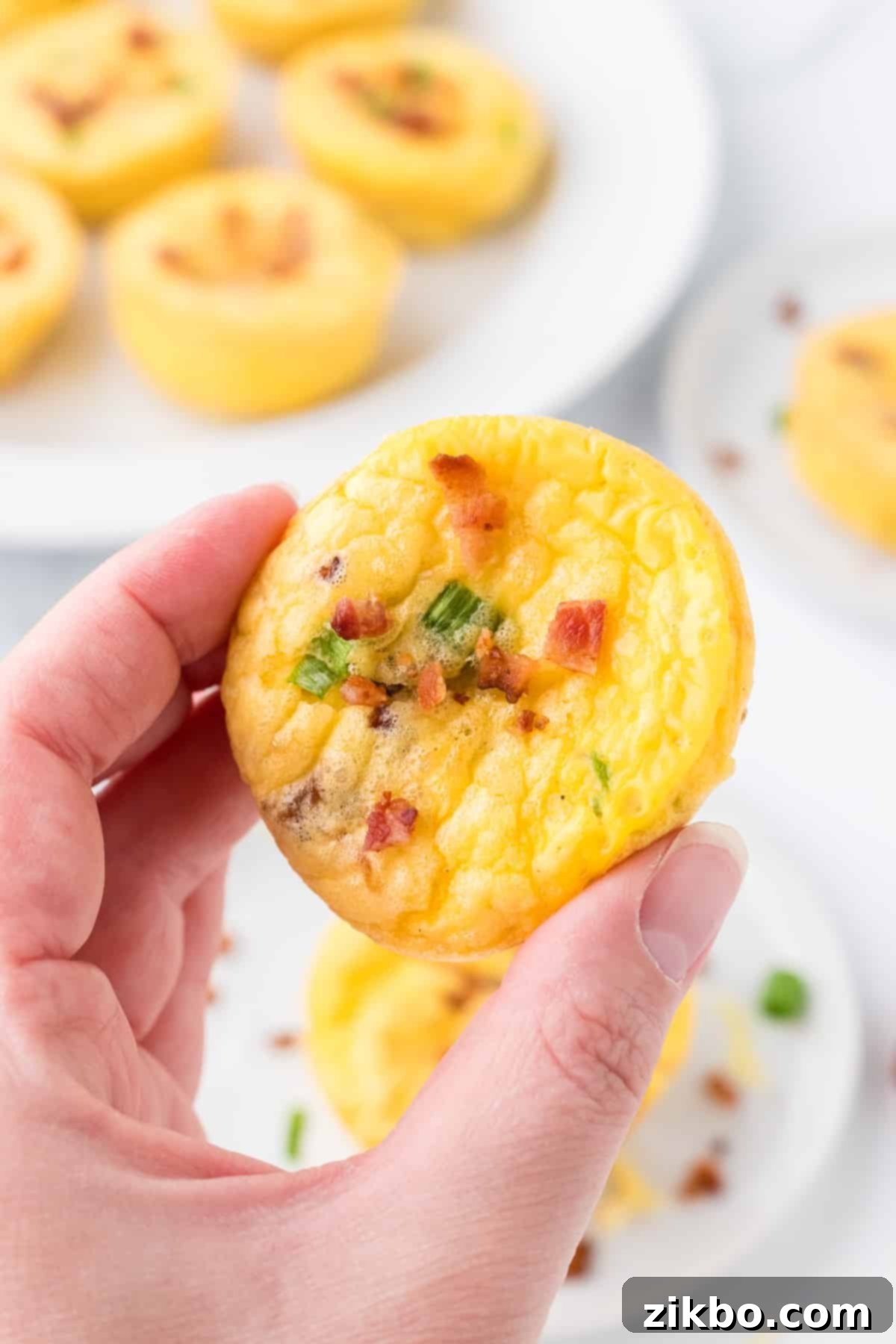 Copycat Starbucks Bacon and Gruyere Egg Bites 8 A hand holding an egg bite garnished with crumbled bacon and green onion.