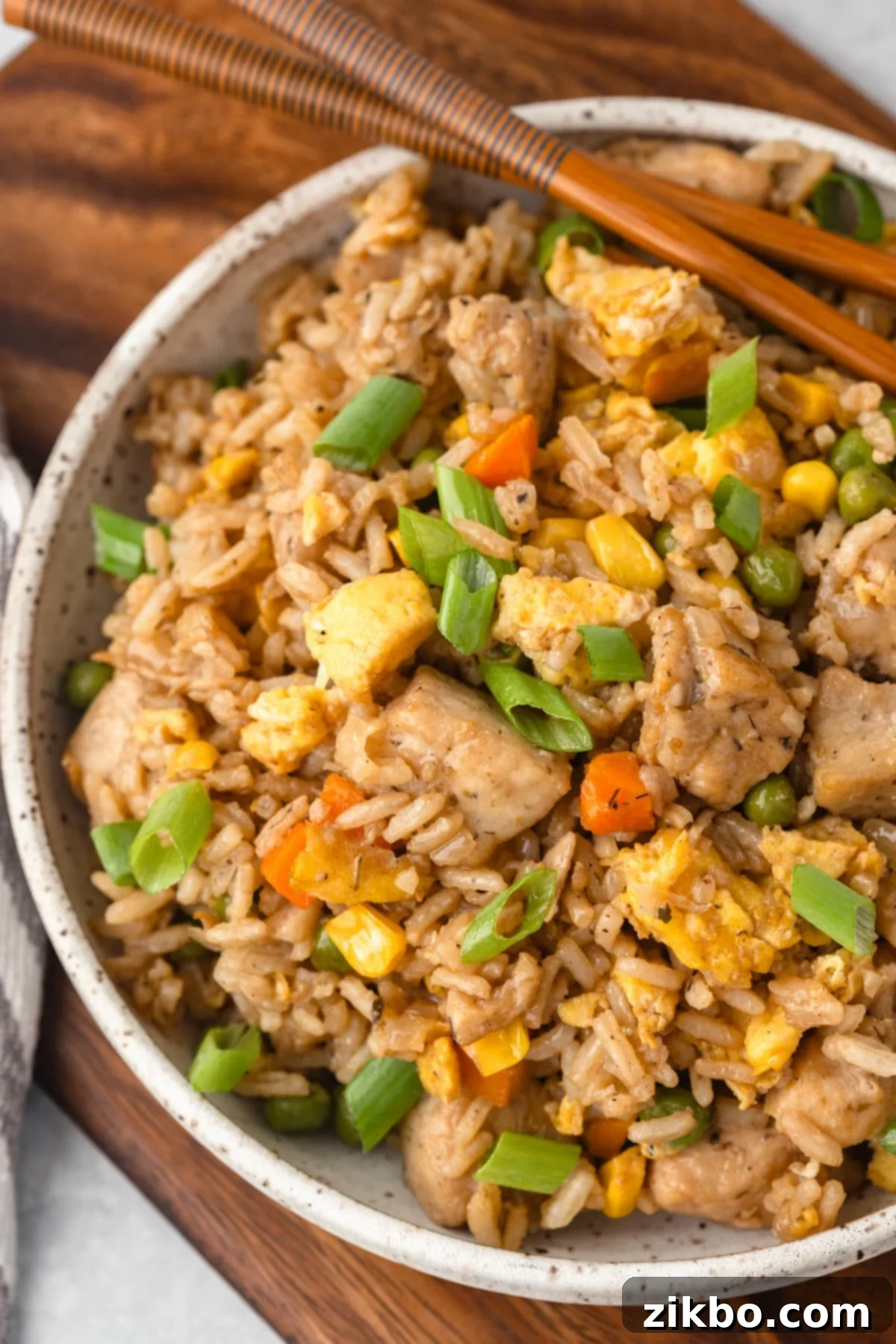 Signature Benihana Chicken Fried Rice 5 A bowl of chicken fried rice with a pair of chopsticks on the side of the bowl.