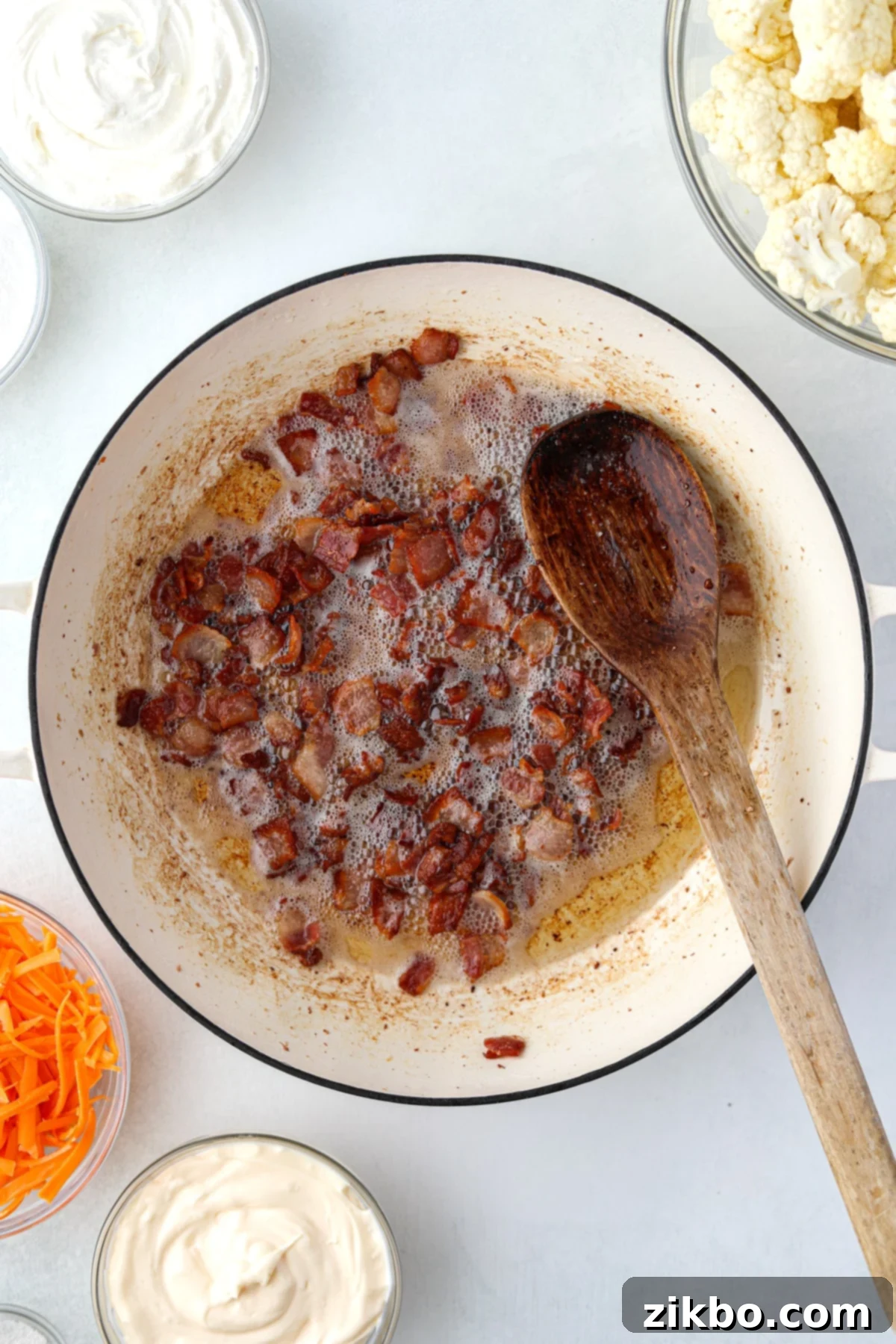 Cooked and crisp bacon pieces draining on paper towels, with an enameled skillet in the background.