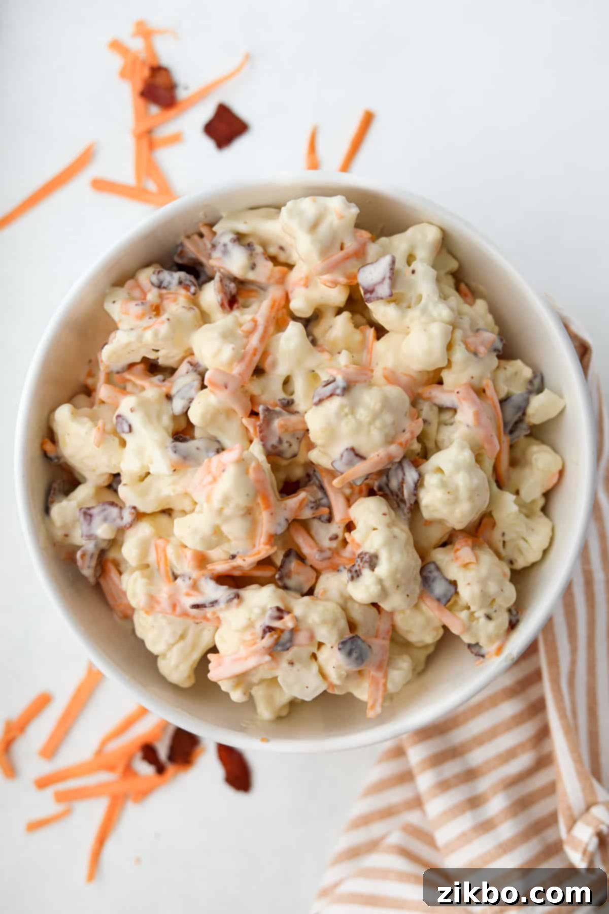 A vibrant bowl of cauliflower salad, generously dotted with crispy bacon pieces and shredded cheddar cheese, ready to be served.