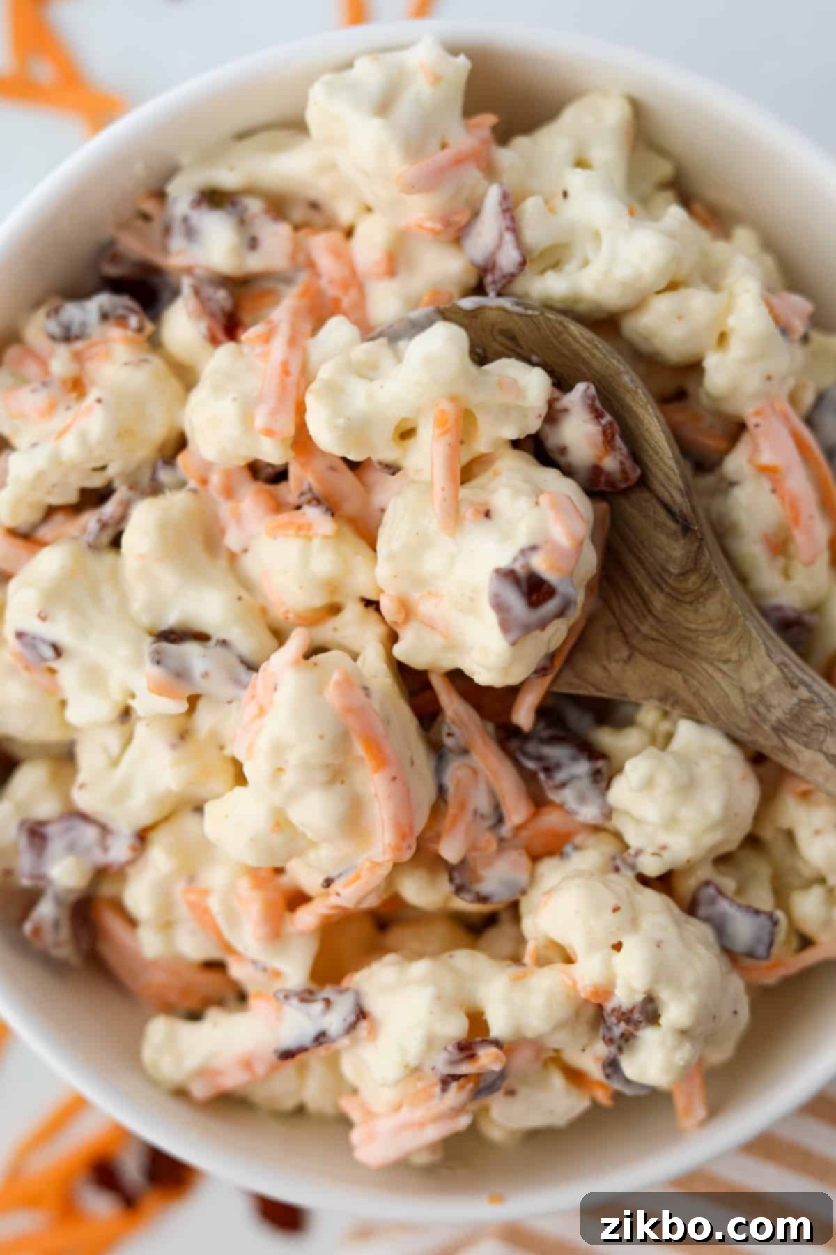 A wooden spoon holding several cauliflower florets generously covered in a creamy dressing, ready to be enjoyed.