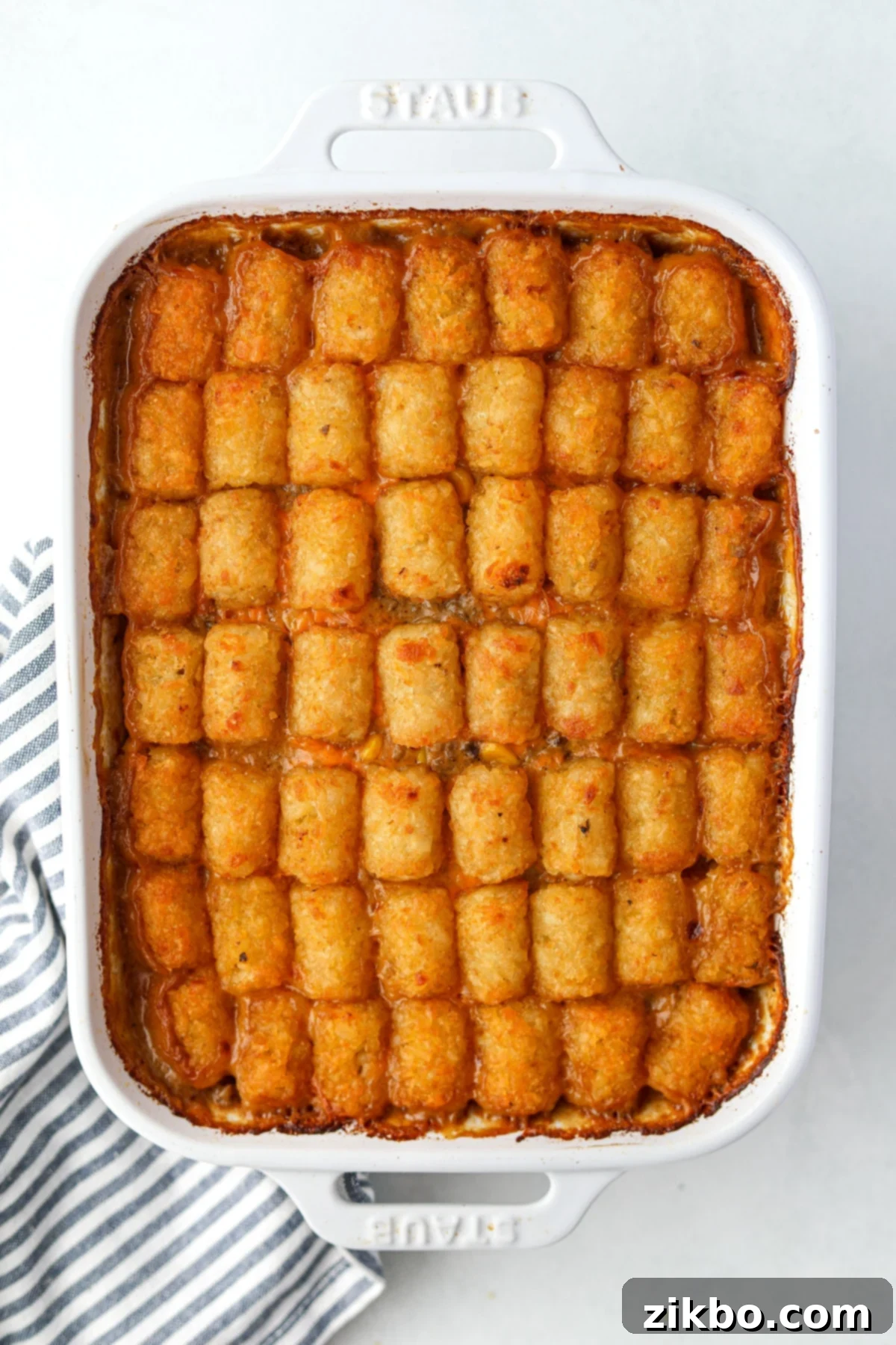 A white baking dish filled with a perfectly baked ground beef and potato tot casserole, golden brown and bubbly.