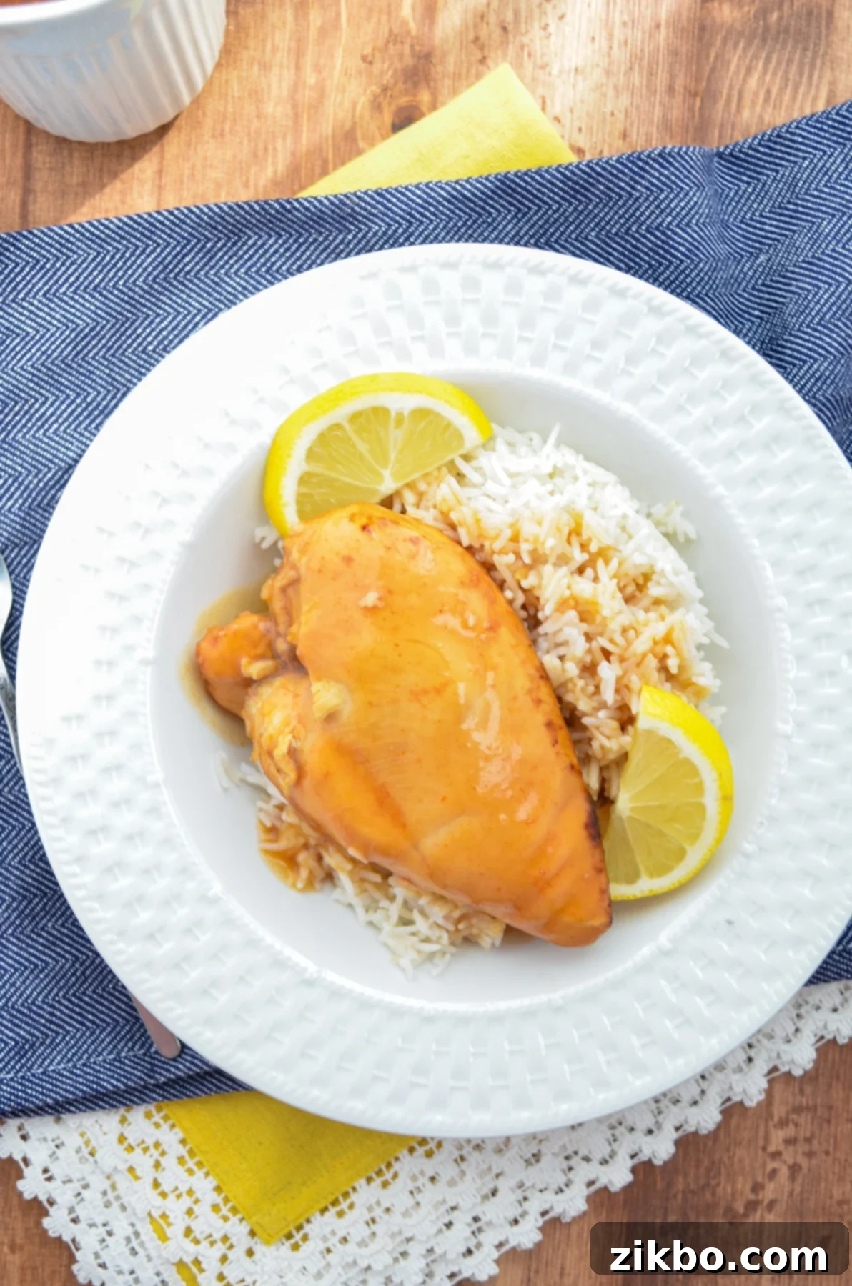 Slow cooker lemonade chicken served over rice with lemon wedges.