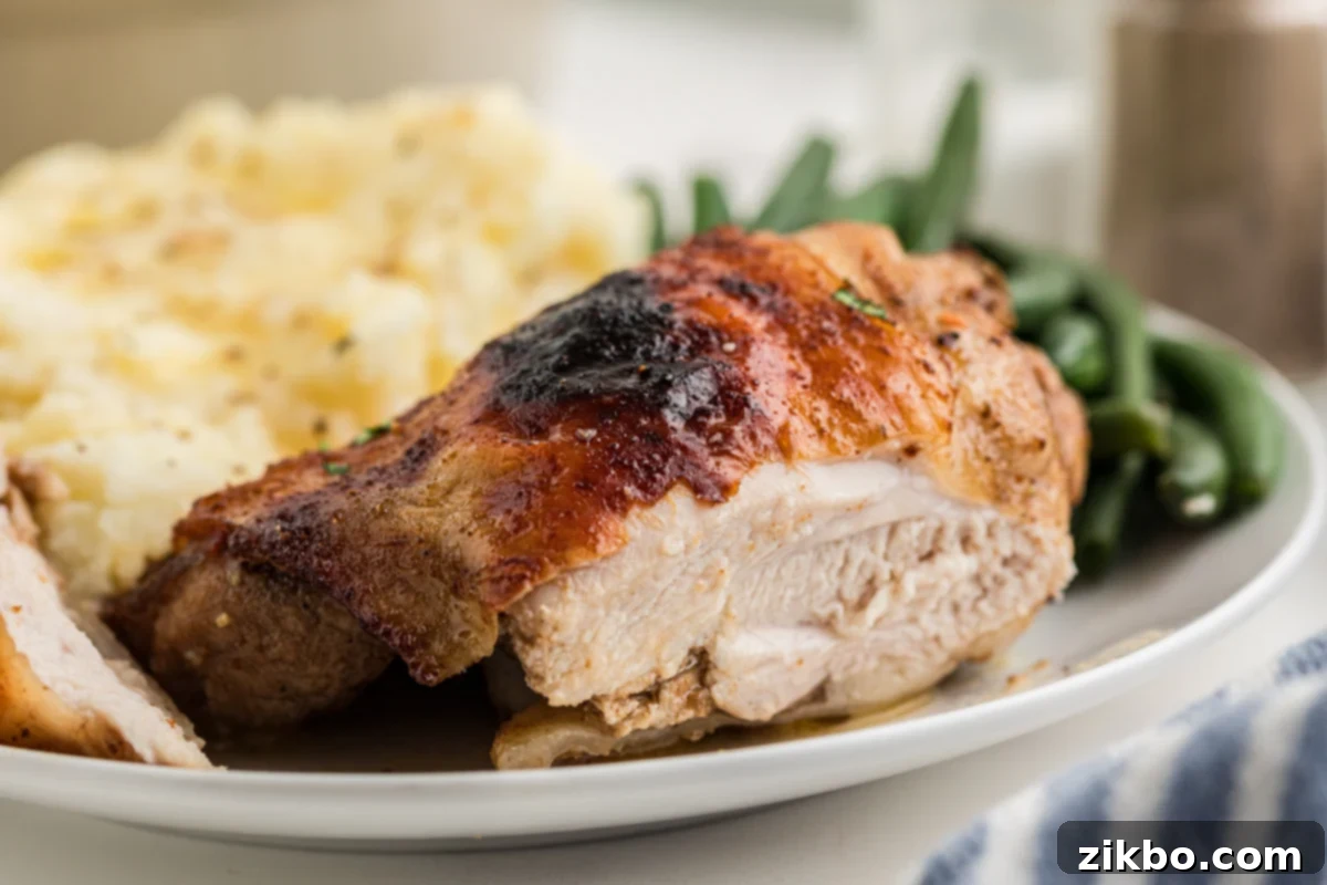 A close up of a chicken thigh served with mashed potato and green beans.
