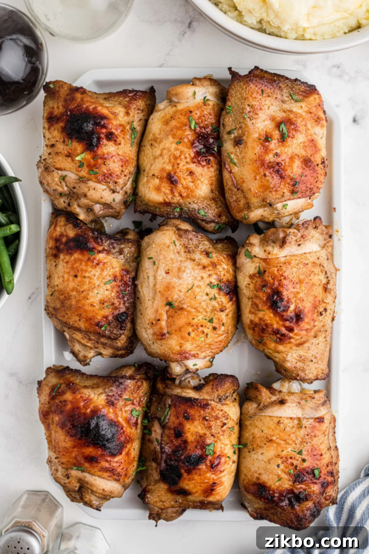 A serving platter filled with 9 chicken thighs that have been baked until crispy, garnished with fresh herbs.