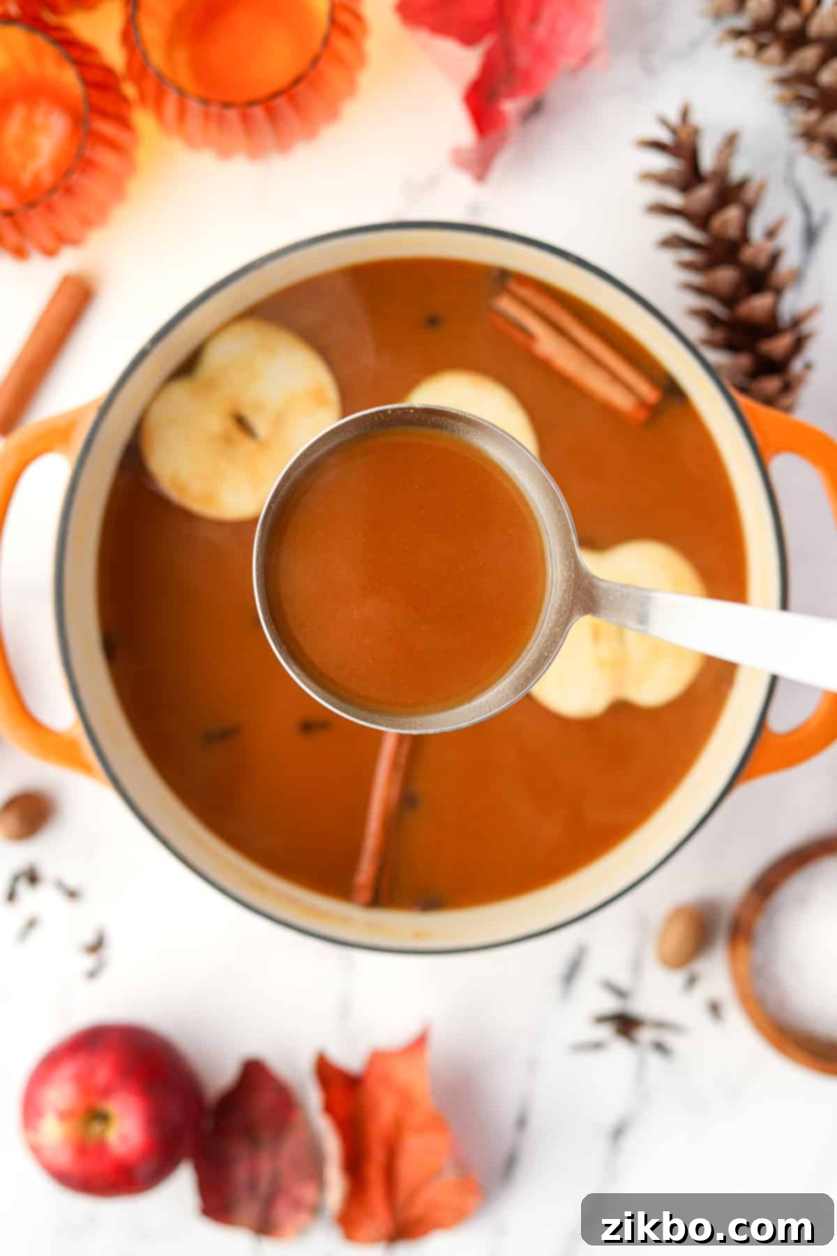 Golden Pumpkin Brew 5 A ladle pulling warm pumpkin apple cider from a Dutch oven, with decorative apple slices and cinnamon sticks floating within the spiced beverage.