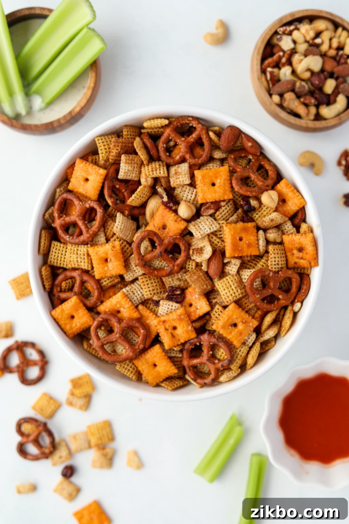 A white bowl filled with homemade snack mix, featuring a mix of Chex cereals, pretzels, and nuts.