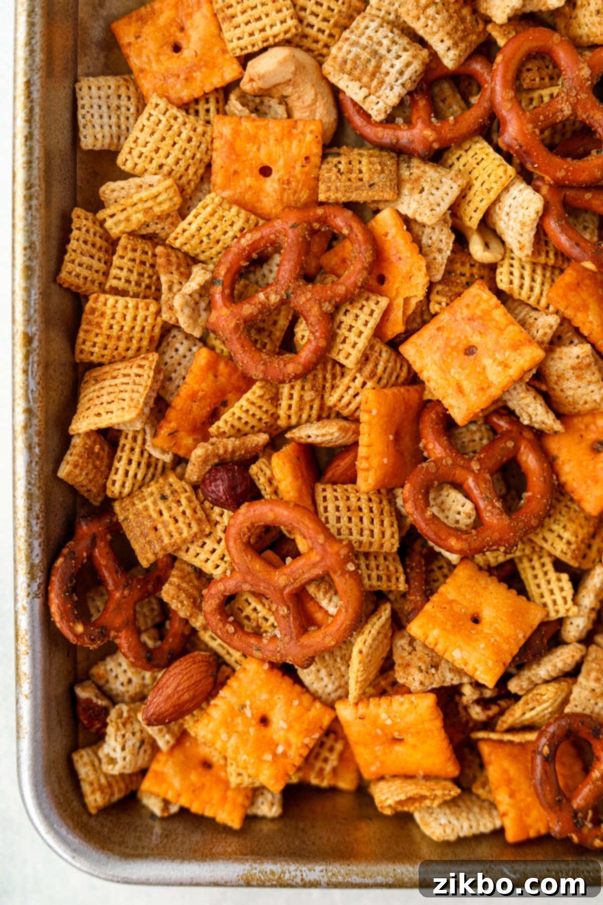 A close up of a baking sheet filled with a homemade snack mix, showing the even coating of seasoning.