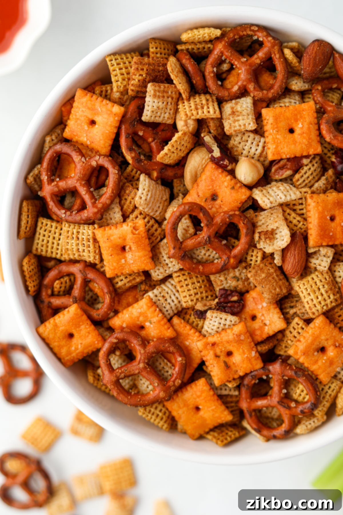 A white bowl filled with snack mix featuring pretzels, chex cereal, nuts, and cheez-its, showcasing the variety of ingredients.