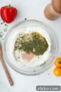 A bowl of Greek yogurt filled with various seasonings, ready to be mixed for ranch.