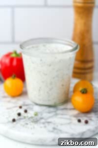 A glass jar filled with homemade ranch dressing, with fresh veggies in the background.