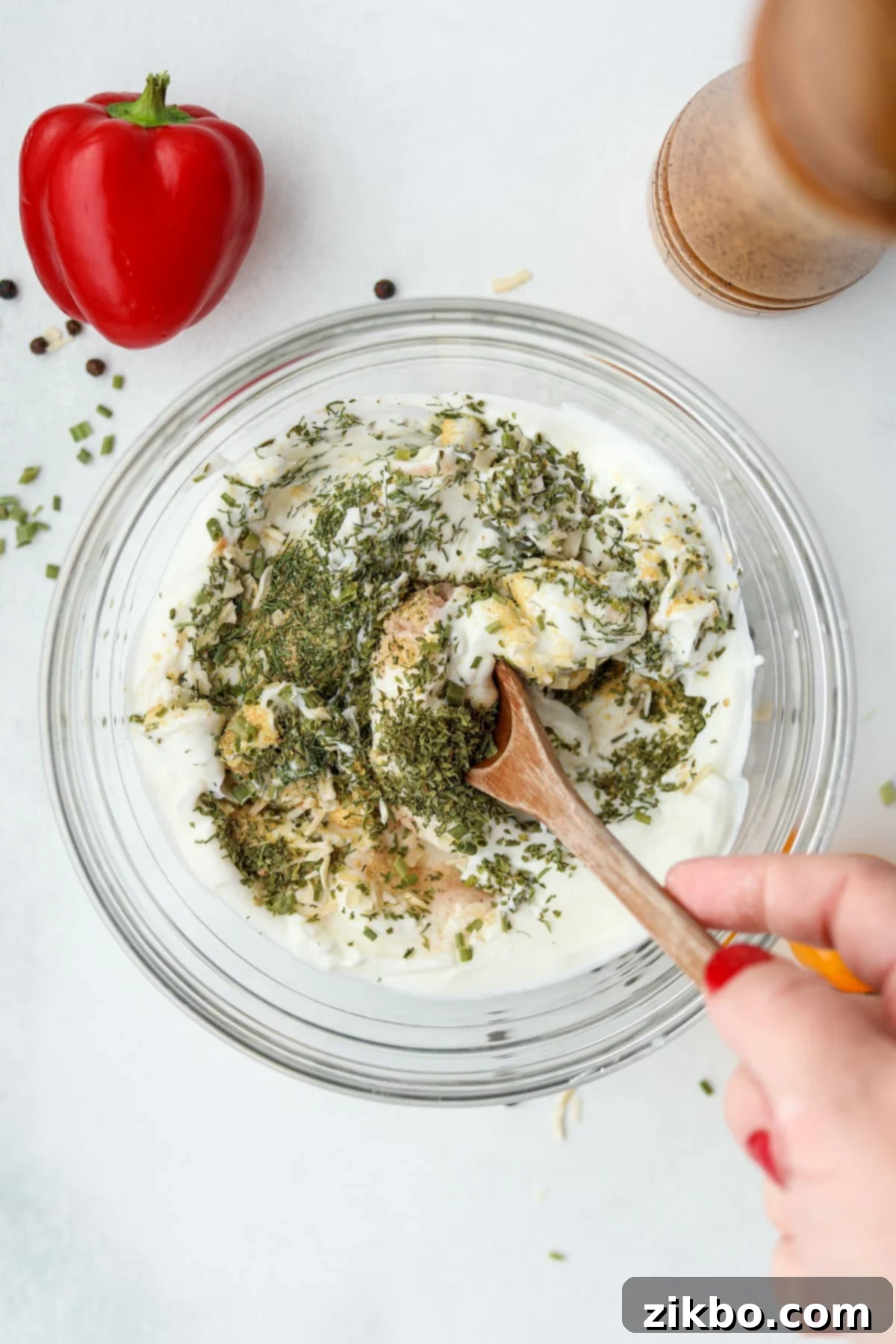 Zesty Greek Ranch Duo 5 A wooden spoon actively stirring the dried seasonings into a bowl of creamy Greek yogurt, beginning the ranch mixing process.