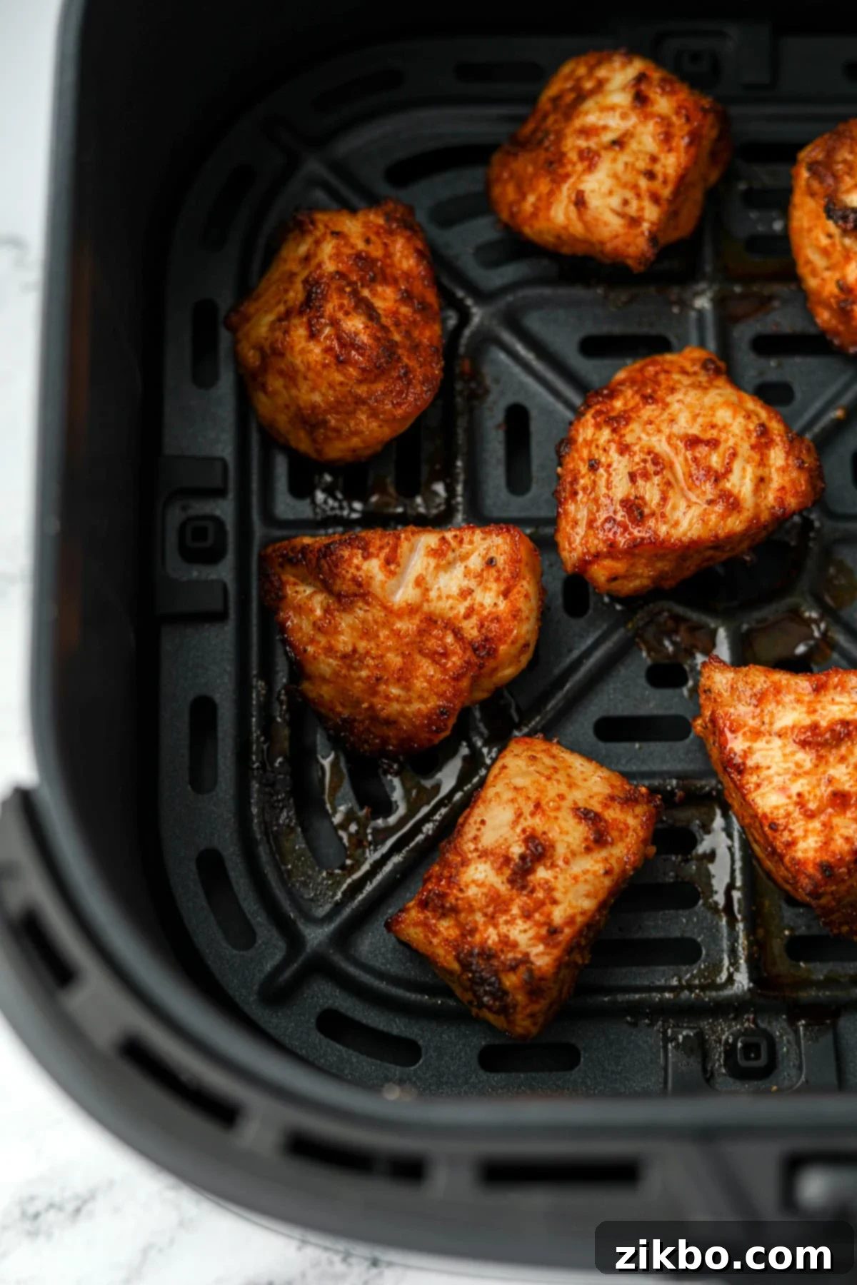 An air fryer basket with several unbreaded chicken nuggets inside.