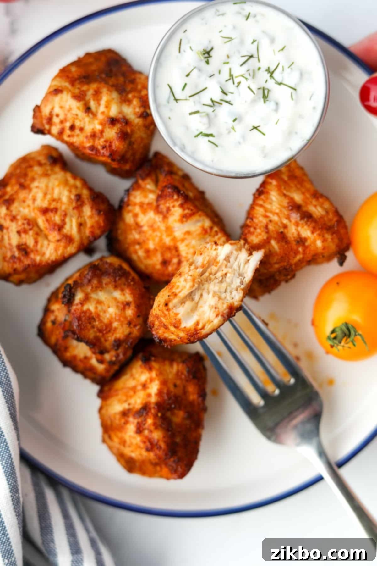 A fork holding up a bite-sized piece of chicken that has been bitten into.