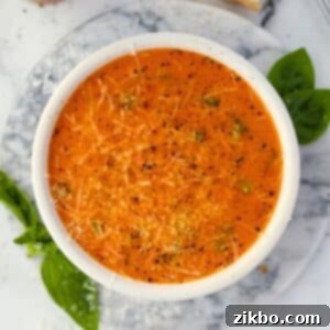 A bowl of cherry tomato soup garnished with parmesan cheese, basil, and cracked black pepper.