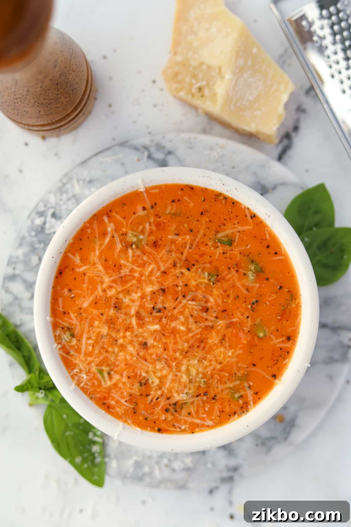 A bowl of tomato soup garnished with basil, parmesan, and cracked black pepper.