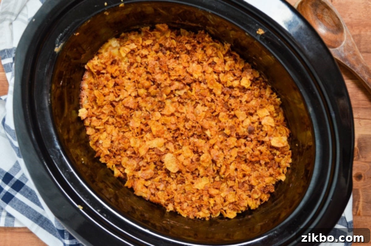 Slow Cooker Golden Cheesy Hash Brown Casserole 2 A slow cooker filled with golden-brown, cheesy hash brown potatoes, glistening with melted cheese and topped generously with crushed, toasted cornflakes.