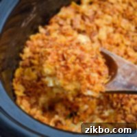 Slow Cooker Golden Cheesy Hash Brown Casserole 11 A large wooden spoon scoops up a portion of funeral potatoes made in a slow cooker.