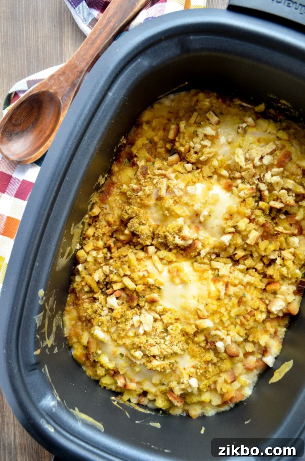 A slow cooker on a wood table, with stuffing and swiss cheese coated chicken on the inside.