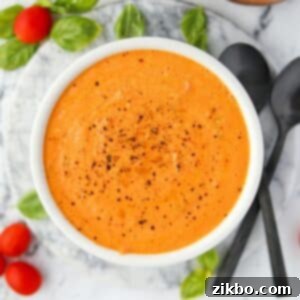 A bowl of cream tomato soup with cherry tomatoes and basil around the outside.