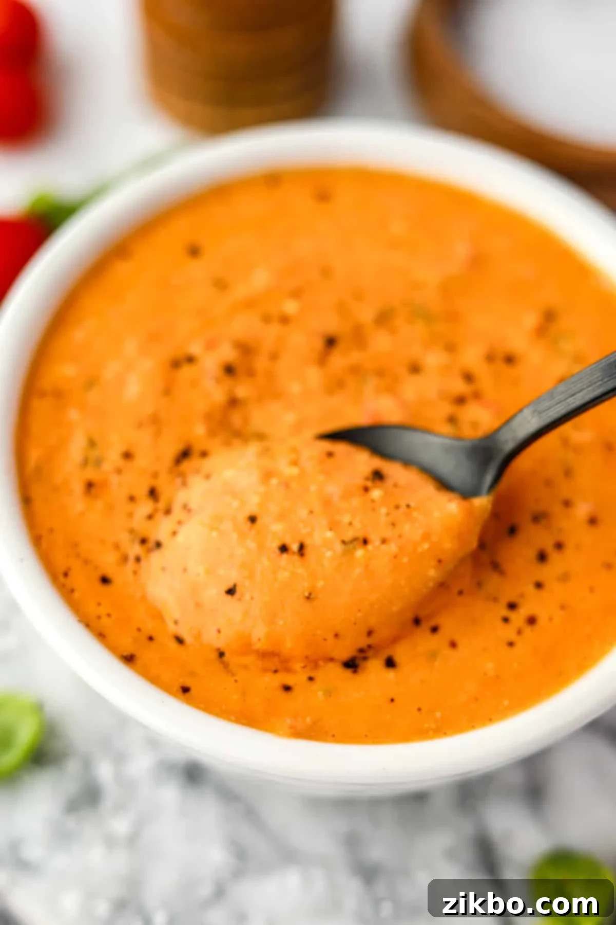 A spoon taking a portion of creamy tomato soup from a bowl.