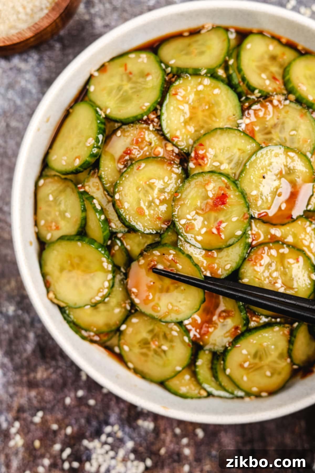Fiery Fresh Cucumber Crunch 2 A bowl of refreshing spicy cucumber salad, garnished with toasted sesame seeds and vibrant chili flakes.