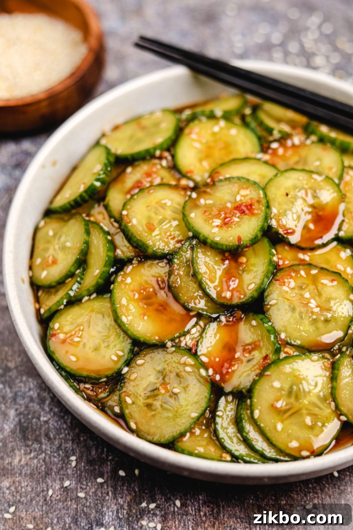 Fiery Fresh Cucumber Crunch 6 A close-up shot of a bowl of spicy cucumber salad, glistening with its rich, brownish-red dressing and adorned with sesame seeds.