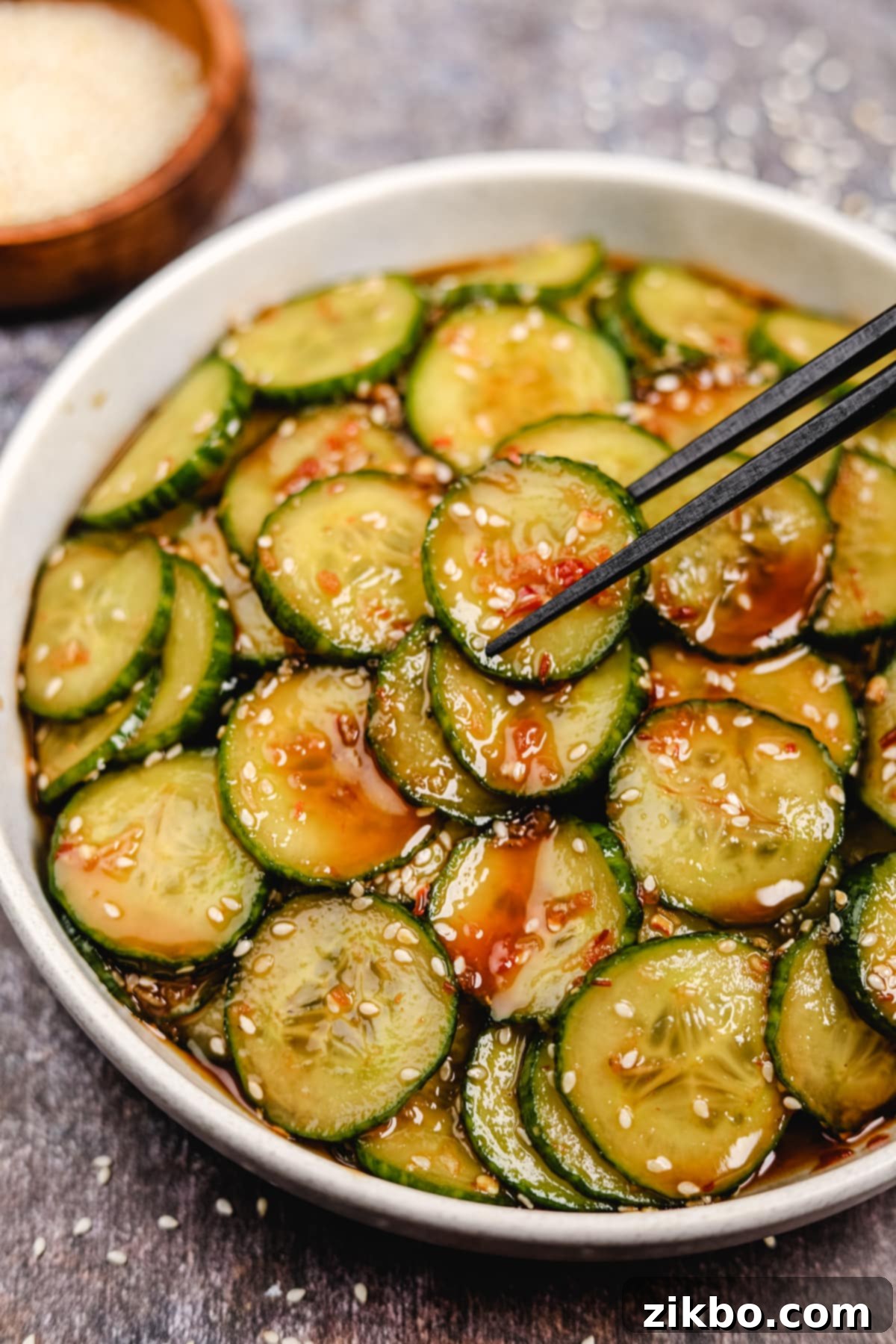 Fiery Fresh Cucumber Crunch 7 Two black chopsticks delicately picking up several marinated cucumber slices from a vibrant bowl of spicy cucumber salad.