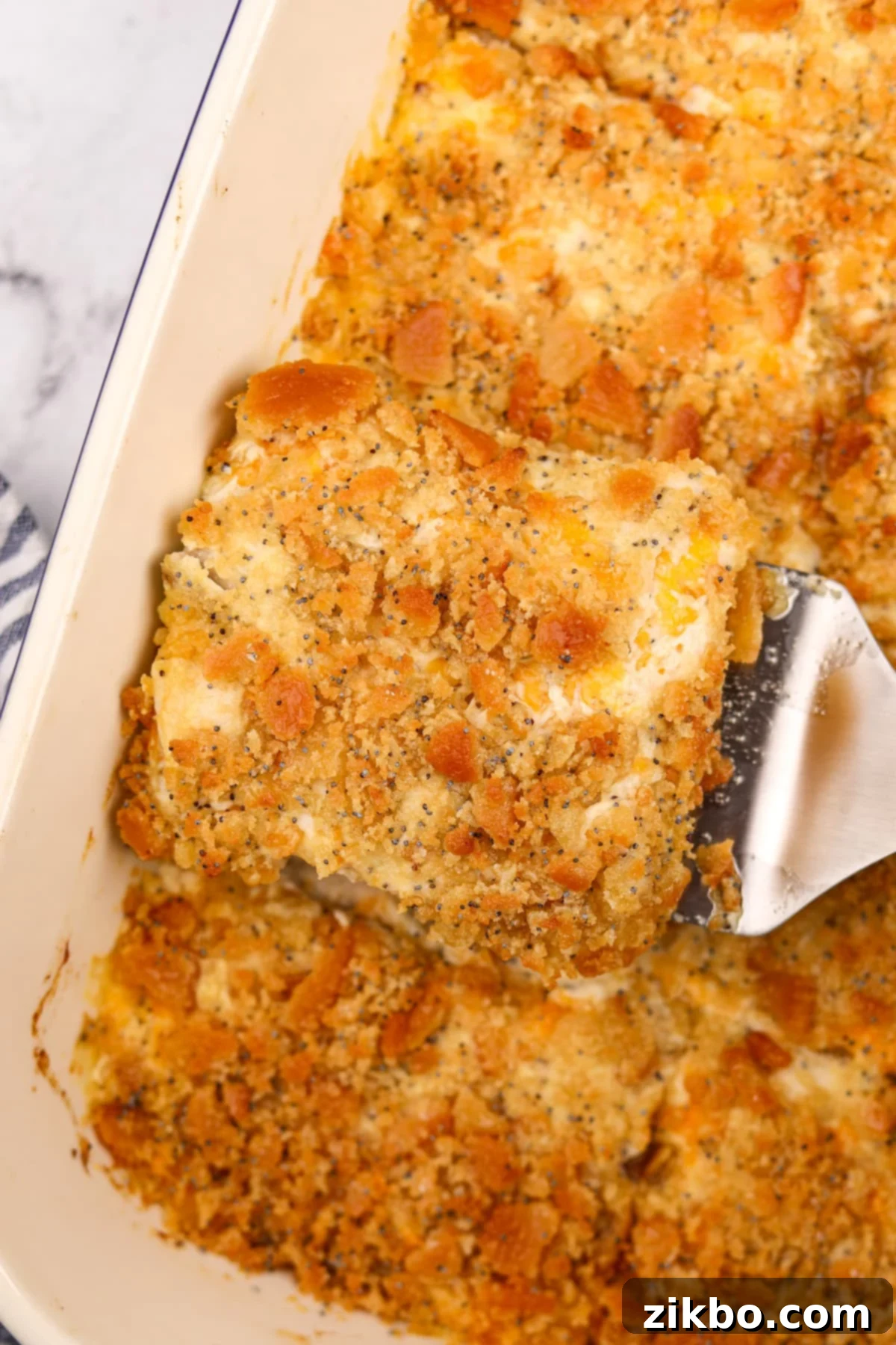 Lifting a portion of poppy seed chicken from a casserole dish.