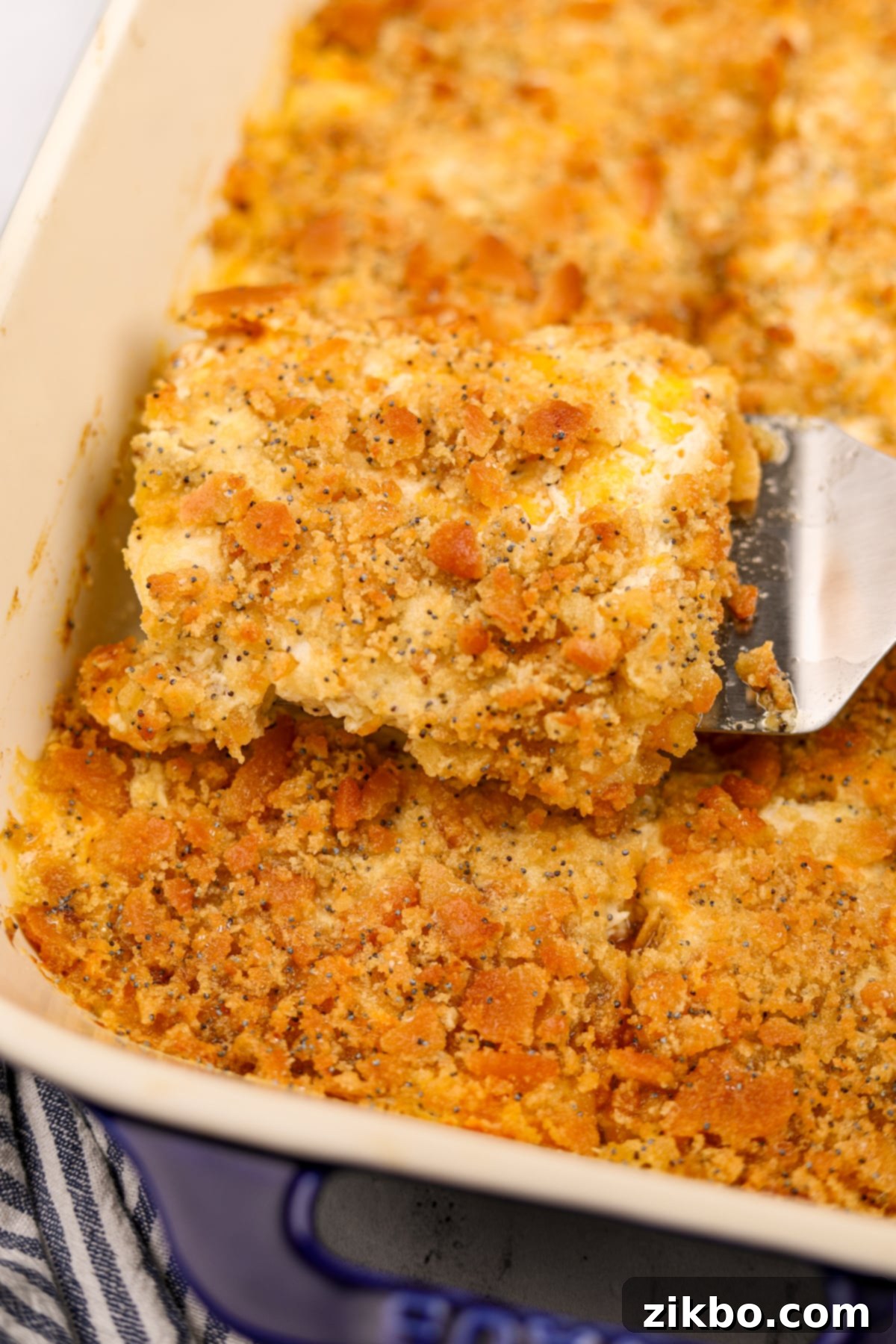 Scooping a creamy casserole from a baking dish; it's topped with a crunchy cracker topping.