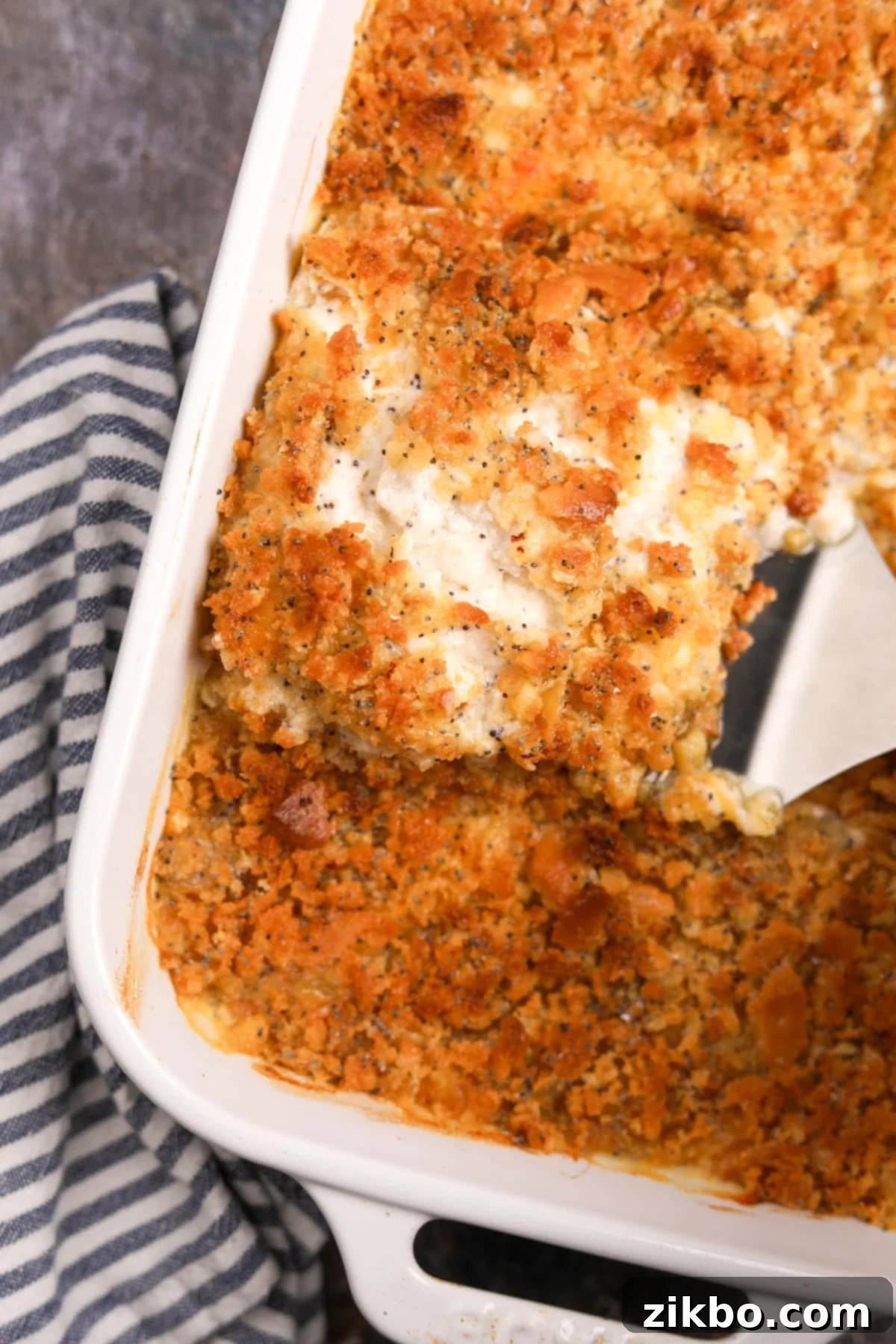 A spatula removing a portion of creamy, golden-brown gluten-free poppy seed chicken casserole from a baking dish, ready to be served.