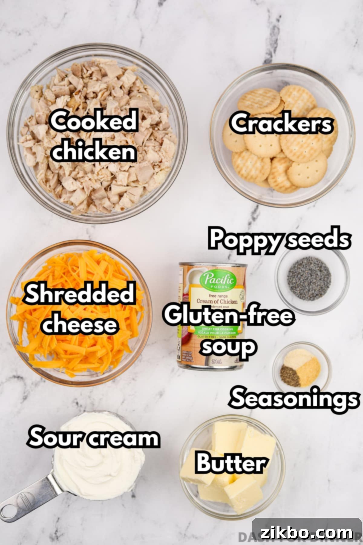 A flat lay of fresh ingredients for gluten-free poppy seed chicken casserole, including shredded cheddar cheese, gluten-free crackers, a stick of butter, a can of gluten-free cream of chicken soup, sour cream, and cooked chicken pieces, all essential for the recipe.
