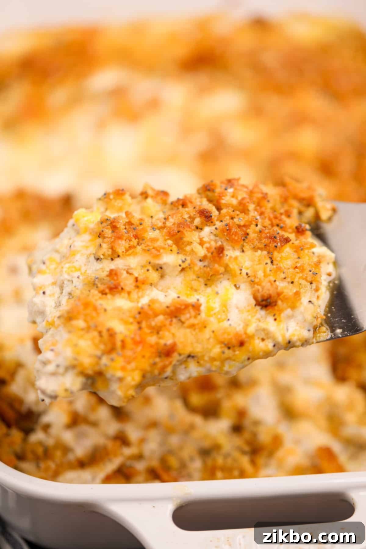 A close-up shot of the finished gluten-free poppy seed chicken casserole, showing its creamy texture bubbling beneath a perfectly golden and crunchy topping speckled with poppy seeds.