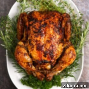 A whole roasted chicken on a white platter, garnished with fresh herbs.