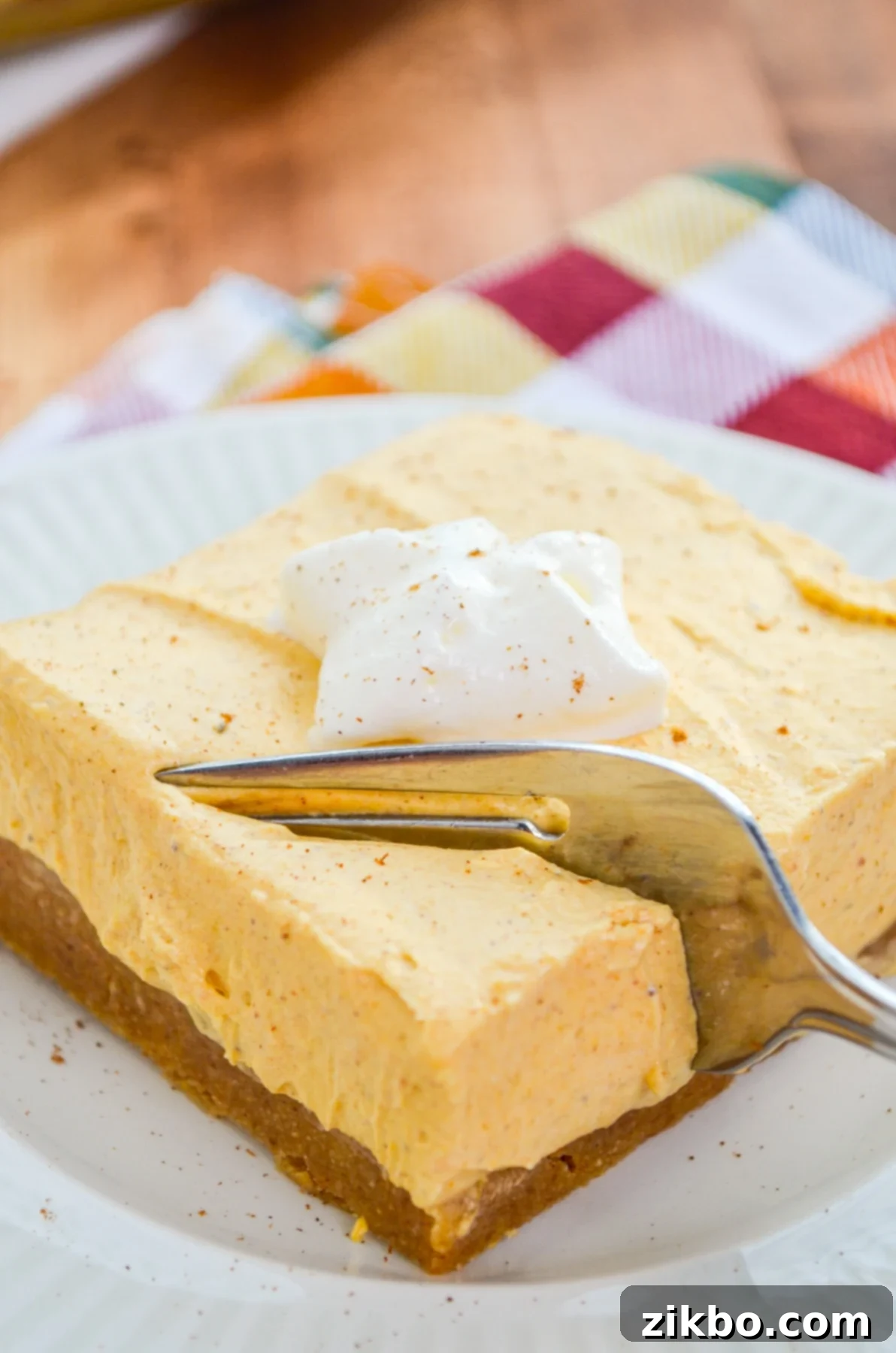 A fork sinking into a pumpkin cheesecake bar, highlighting the soft and creamy texture.